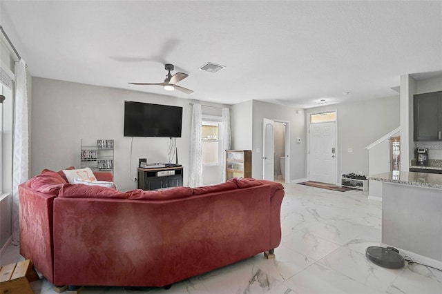 living area with a ceiling fan, marble finish floor, visible vents, and baseboards