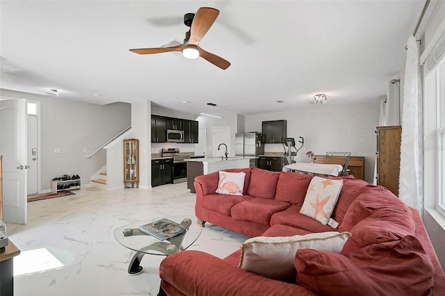 living area featuring stairs, marble finish floor, ceiling fan, and baseboards