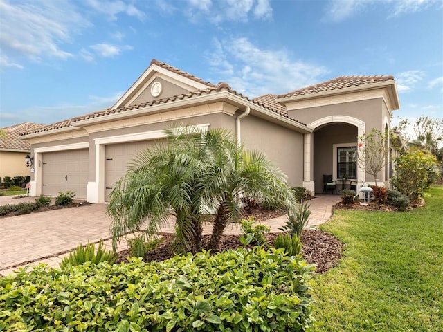 mediterranean / spanish house with stucco siding, a front lawn, a tile roof, decorative driveway, and a garage