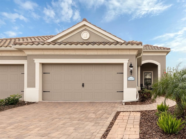 view of front of property with stucco siding, a tiled roof, decorative driveway, and a garage