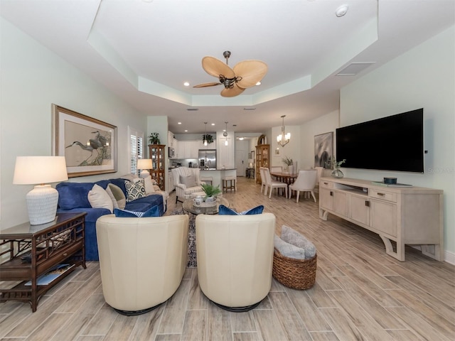 living area with recessed lighting, ceiling fan with notable chandelier, a tray ceiling, and wood tiled floor