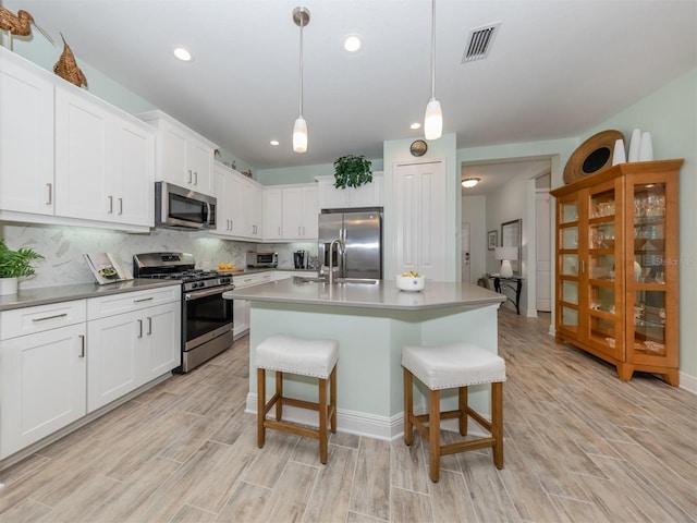 kitchen with visible vents, a breakfast bar, a sink, decorative backsplash, and appliances with stainless steel finishes