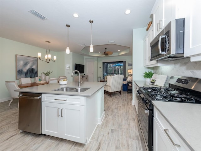 kitchen featuring visible vents, a sink, a tray ceiling, tasteful backsplash, and stainless steel appliances