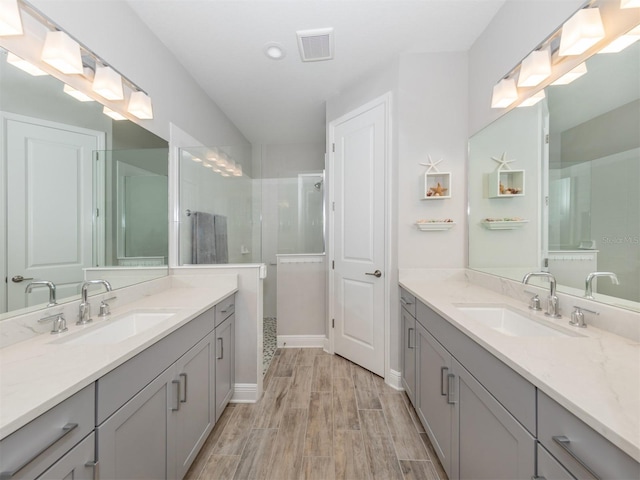 full bath featuring a sink, visible vents, wood finished floors, and a shower stall