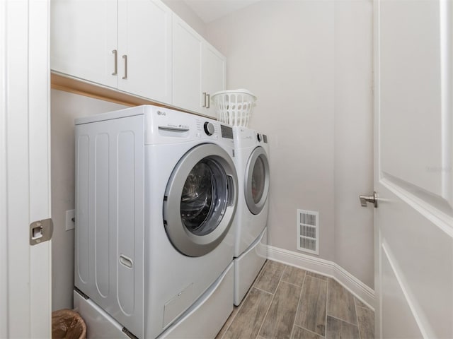 washroom with visible vents, cabinet space, wood tiled floor, and washing machine and clothes dryer