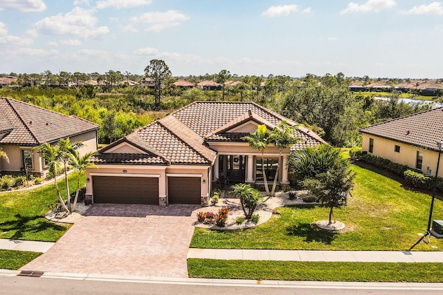 mediterranean / spanish house featuring a front lawn, a tiled roof, stucco siding, a garage, and driveway