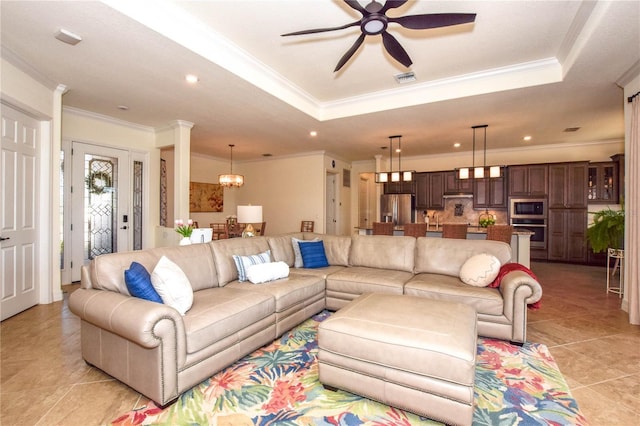 living room with a tray ceiling, light tile patterned flooring, recessed lighting, crown molding, and ceiling fan with notable chandelier