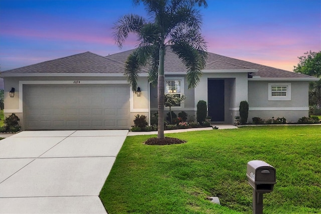 ranch-style home featuring a garage, concrete driveway, a lawn, roof with shingles, and stucco siding