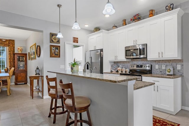 kitchen with a center island with sink, backsplash, appliances with stainless steel finishes, white cabinets, and light tile patterned flooring