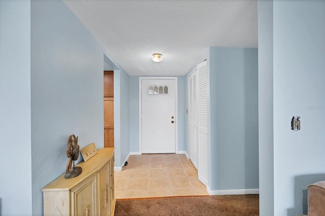 corridor with a textured ceiling, light carpet, light tile patterned flooring, and baseboards