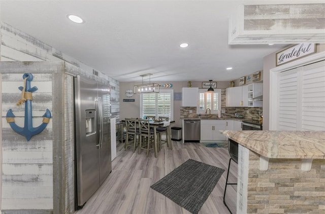 kitchen featuring white cabinets, appliances with stainless steel finishes, backsplash, light wood-type flooring, and a sink