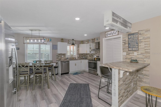 kitchen featuring decorative backsplash, wall chimney exhaust hood, stainless steel appliances, white cabinetry, and a sink