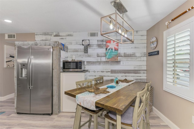 dining room featuring a healthy amount of sunlight, wooden walls, an accent wall, and visible vents