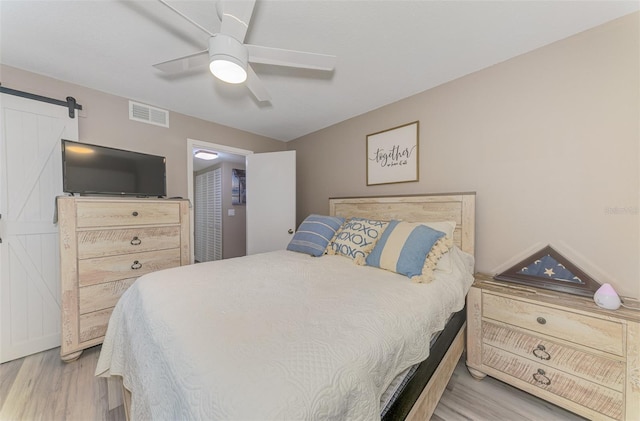 bedroom featuring light wood-type flooring, a barn door, visible vents, and ceiling fan