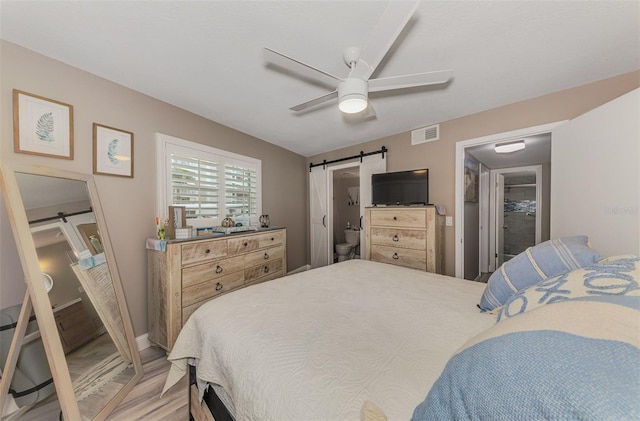 bedroom with a barn door, light wood-type flooring, visible vents, and a ceiling fan