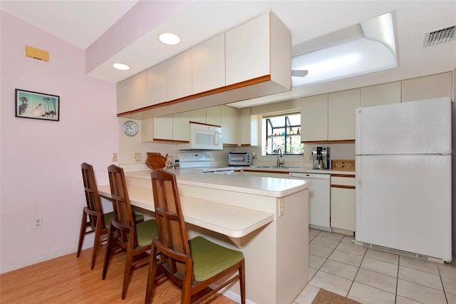 kitchen with a breakfast bar, light countertops, visible vents, white appliances, and a peninsula