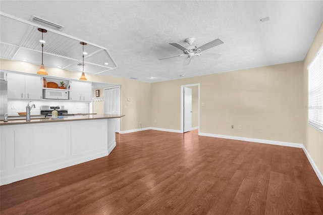 unfurnished living room featuring a ceiling fan, a textured ceiling, baseboards, visible vents, and dark wood-type flooring
