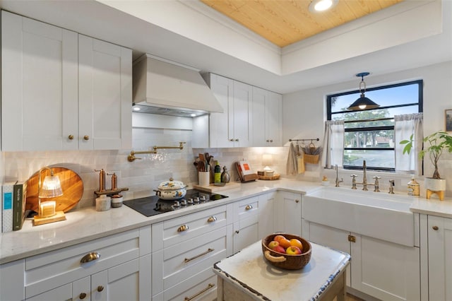 kitchen with backsplash, black electric stovetop, a tray ceiling, custom range hood, and a sink