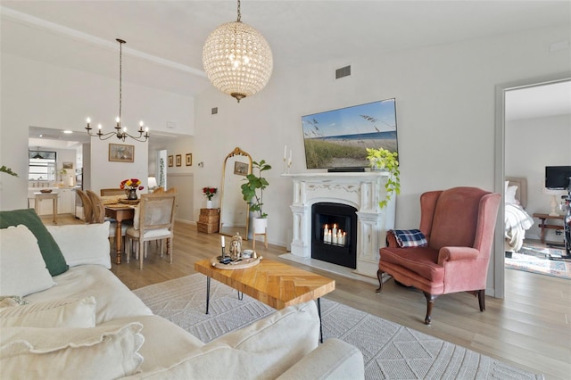 living room with a chandelier, a fireplace with flush hearth, light wood-style flooring, and visible vents