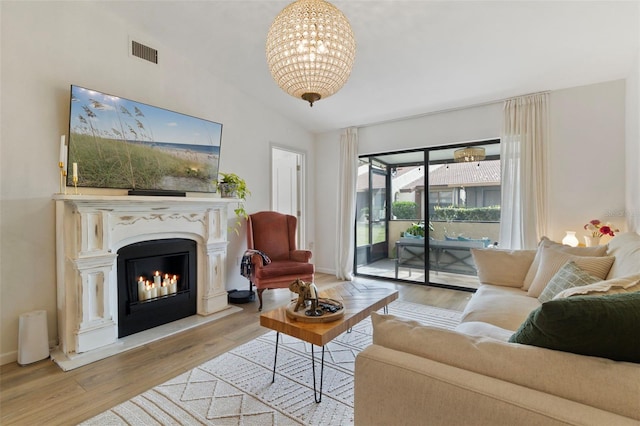 living room with a glass covered fireplace, lofted ceiling, wood finished floors, and visible vents