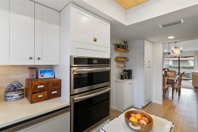 kitchen with tasteful backsplash, visible vents, a chandelier, light wood-style flooring, and stainless steel double oven