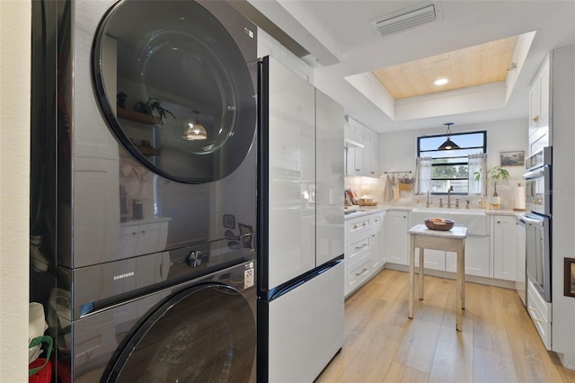 washroom with laundry area, a sink, visible vents, stacked washer / drying machine, and light wood finished floors