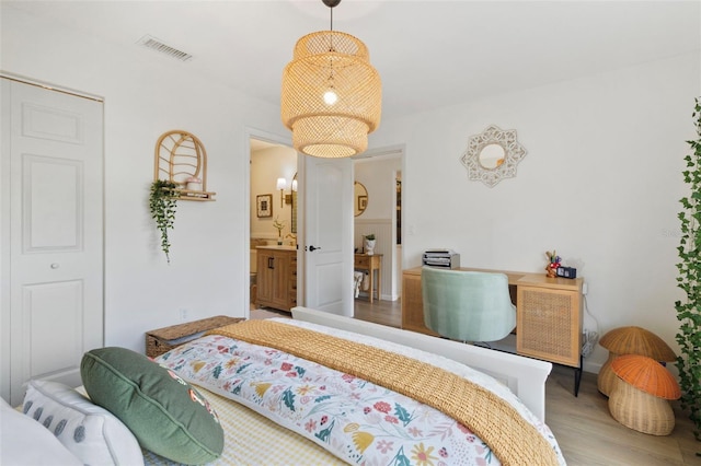 bedroom with wood finished floors, visible vents, and ensuite bathroom