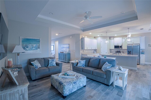 living room with ceiling fan, a raised ceiling, wood finished floors, and ornamental molding