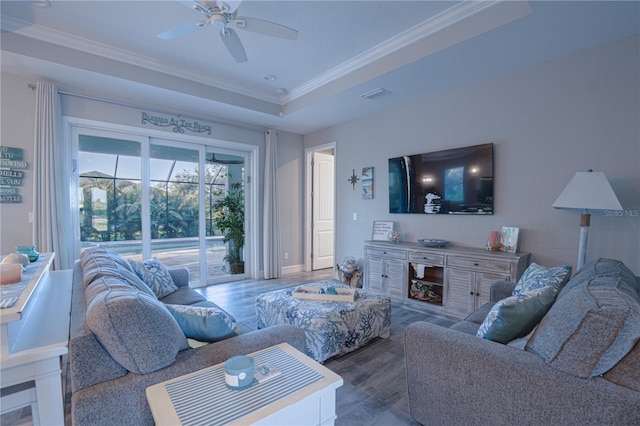 living area with a ceiling fan, wood finished floors, visible vents, crown molding, and a raised ceiling