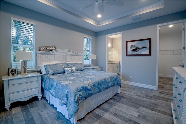 bedroom with a walk in closet, ornamental molding, a tray ceiling, baseboards, and dark wood-style flooring