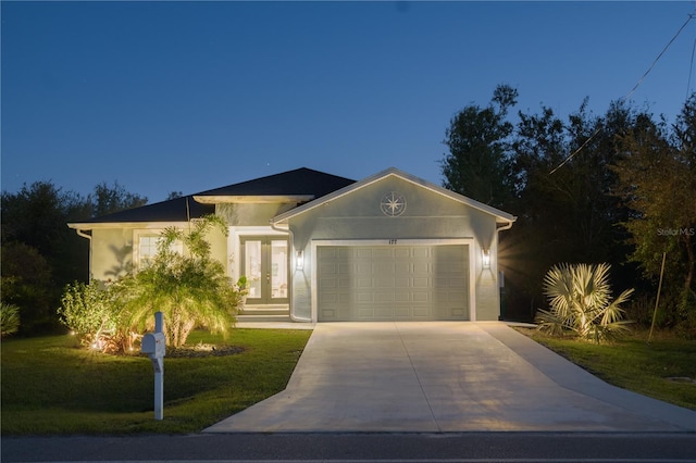 view of front facade featuring stucco siding, driveway, a front lawn, french doors, and an attached garage