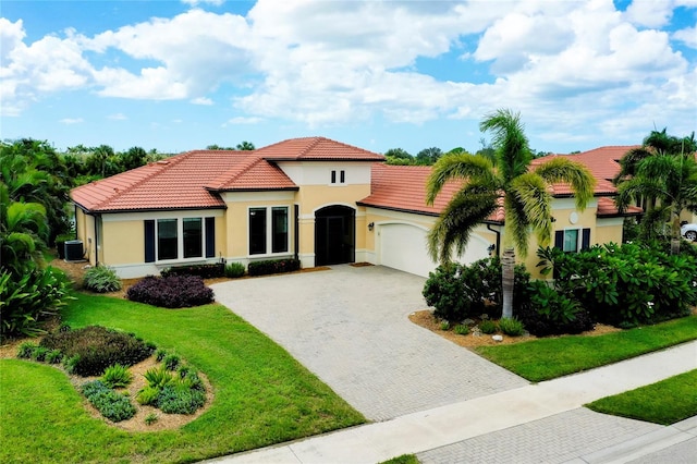 mediterranean / spanish-style house featuring a tiled roof, an attached garage, decorative driveway, a front lawn, and stucco siding