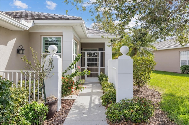 entrance to property featuring a tile roof, fence, a lawn, and stucco siding