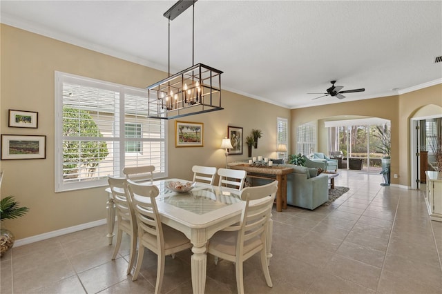 dining room with light tile patterned floors, baseboards, arched walkways, ceiling fan, and ornamental molding