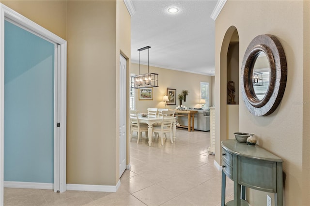 hall with light tile patterned floors, a textured ceiling, a notable chandelier, baseboards, and crown molding