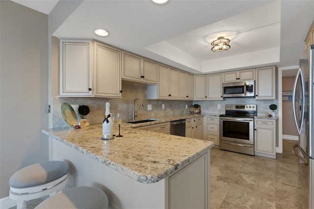 kitchen featuring a tray ceiling, stainless steel appliances, decorative backsplash, a sink, and a peninsula