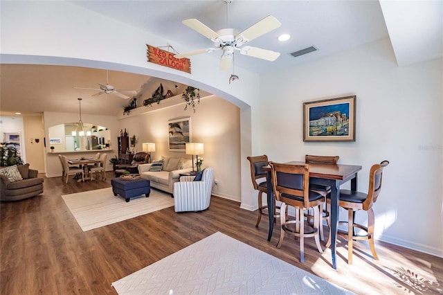 living area featuring baseboards, visible vents, arched walkways, wood finished floors, and ceiling fan with notable chandelier