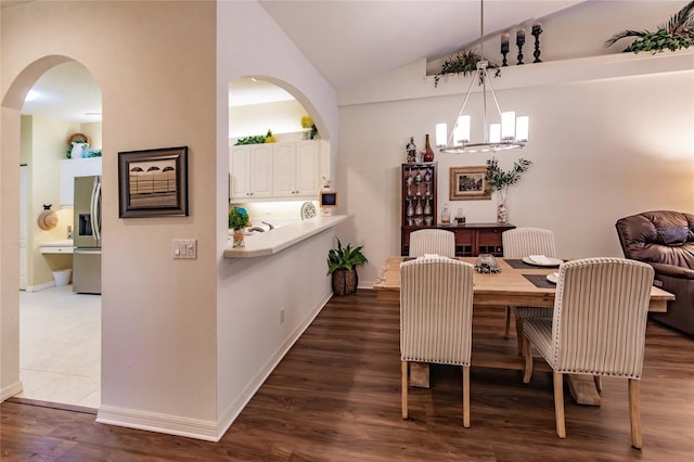 dining area with lofted ceiling, an inviting chandelier, arched walkways, and dark wood-type flooring