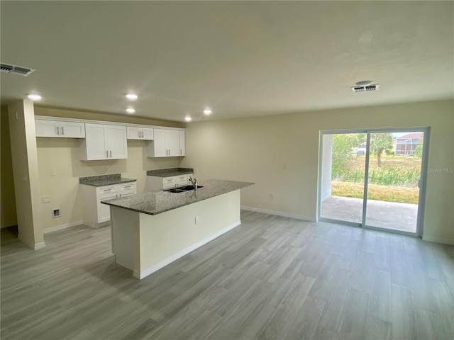 kitchen featuring an island with sink, visible vents, white cabinets, and a sink