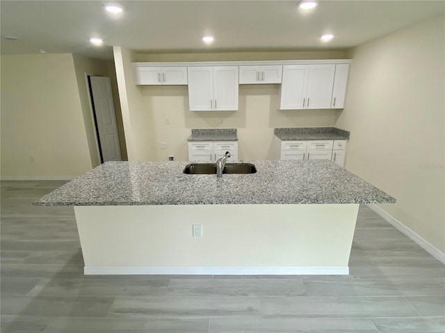 kitchen featuring stone counters, a kitchen island with sink, white cabinets, and a sink