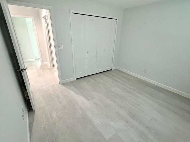 unfurnished bedroom with light wood-style floors, a closet, and baseboards