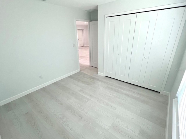 unfurnished bedroom with a closet, light wood-type flooring, and baseboards