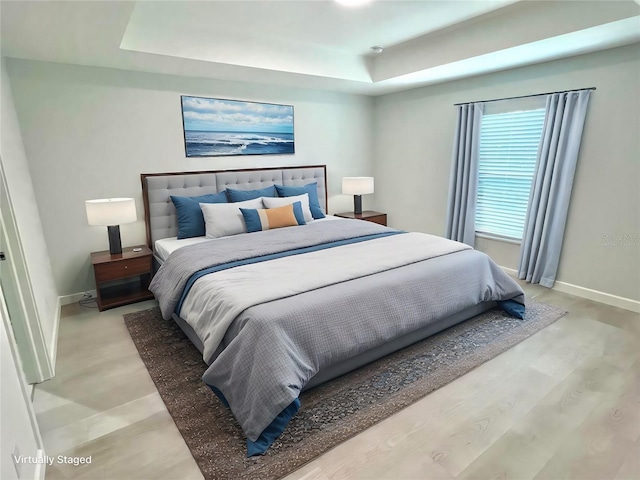 bedroom featuring light wood-style flooring, baseboards, and a raised ceiling