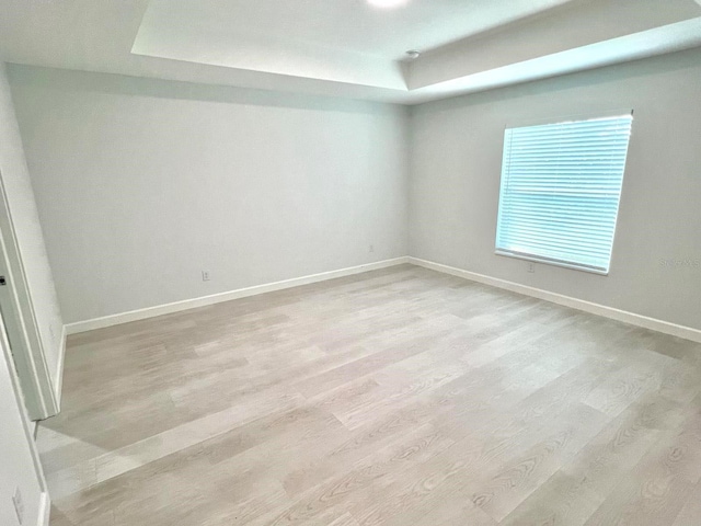 spare room with a tray ceiling, baseboards, and wood finished floors