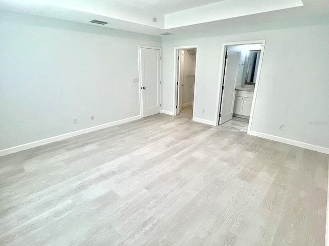 unfurnished bedroom with ensuite bathroom, light wood-style flooring, visible vents, baseboards, and a spacious closet