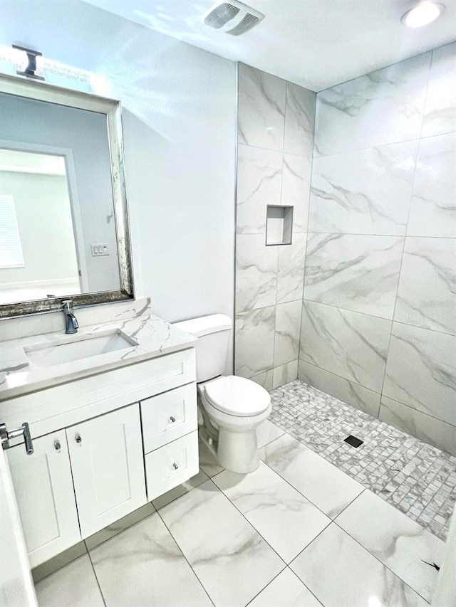 bathroom with toilet, vanity, visible vents, marble finish floor, and tiled shower