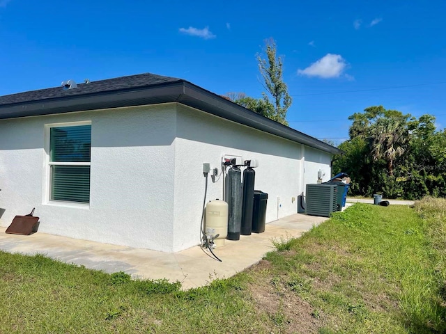 view of side of property featuring roof with shingles, a lawn, cooling unit, and stucco siding