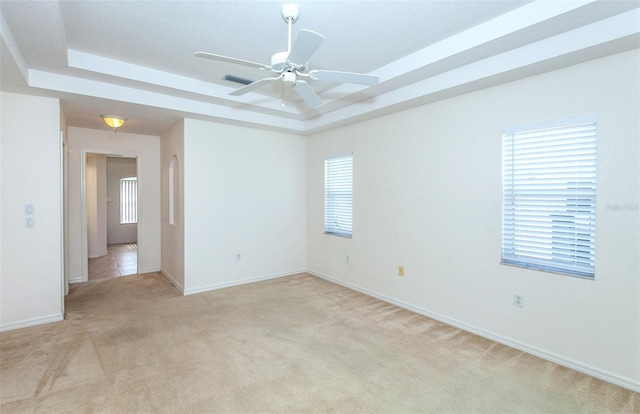 spare room featuring visible vents, baseboards, a raised ceiling, a ceiling fan, and light colored carpet