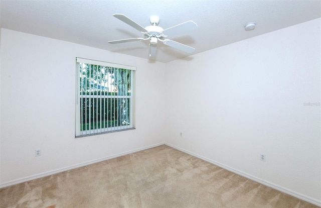 empty room with a ceiling fan, light colored carpet, and baseboards