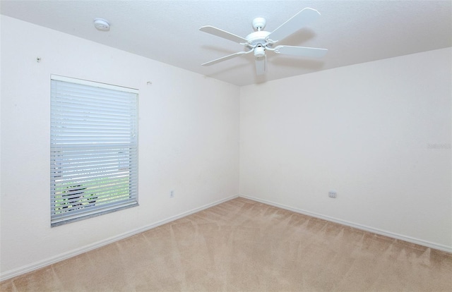 empty room featuring a ceiling fan, light colored carpet, and baseboards